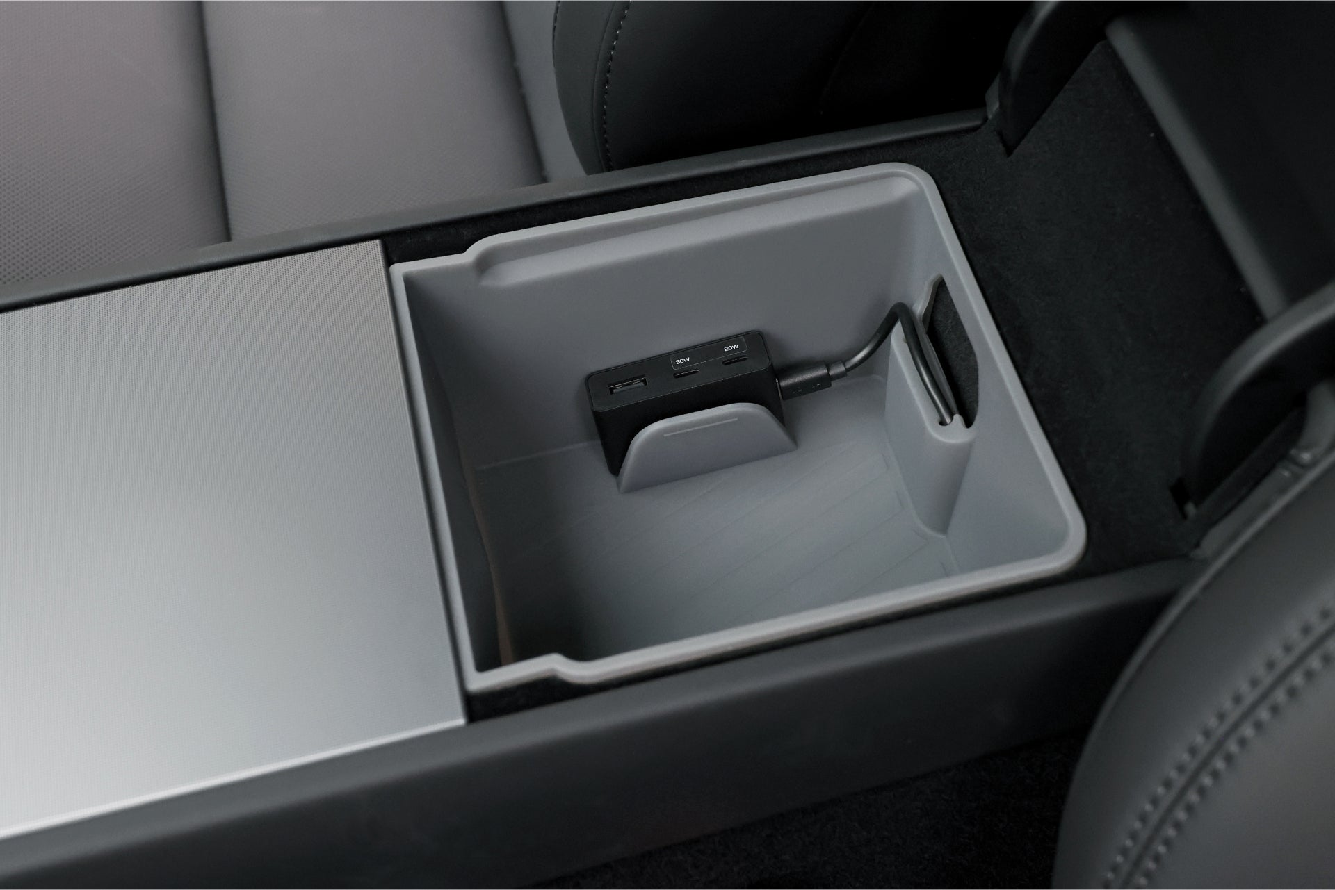 The image depicts the interior of a car's center console with a JOWUA Power HUB USB hub featuring multiple charging ports, nestled in a compact gray tray. The surrounding area is upholstered in dark material.