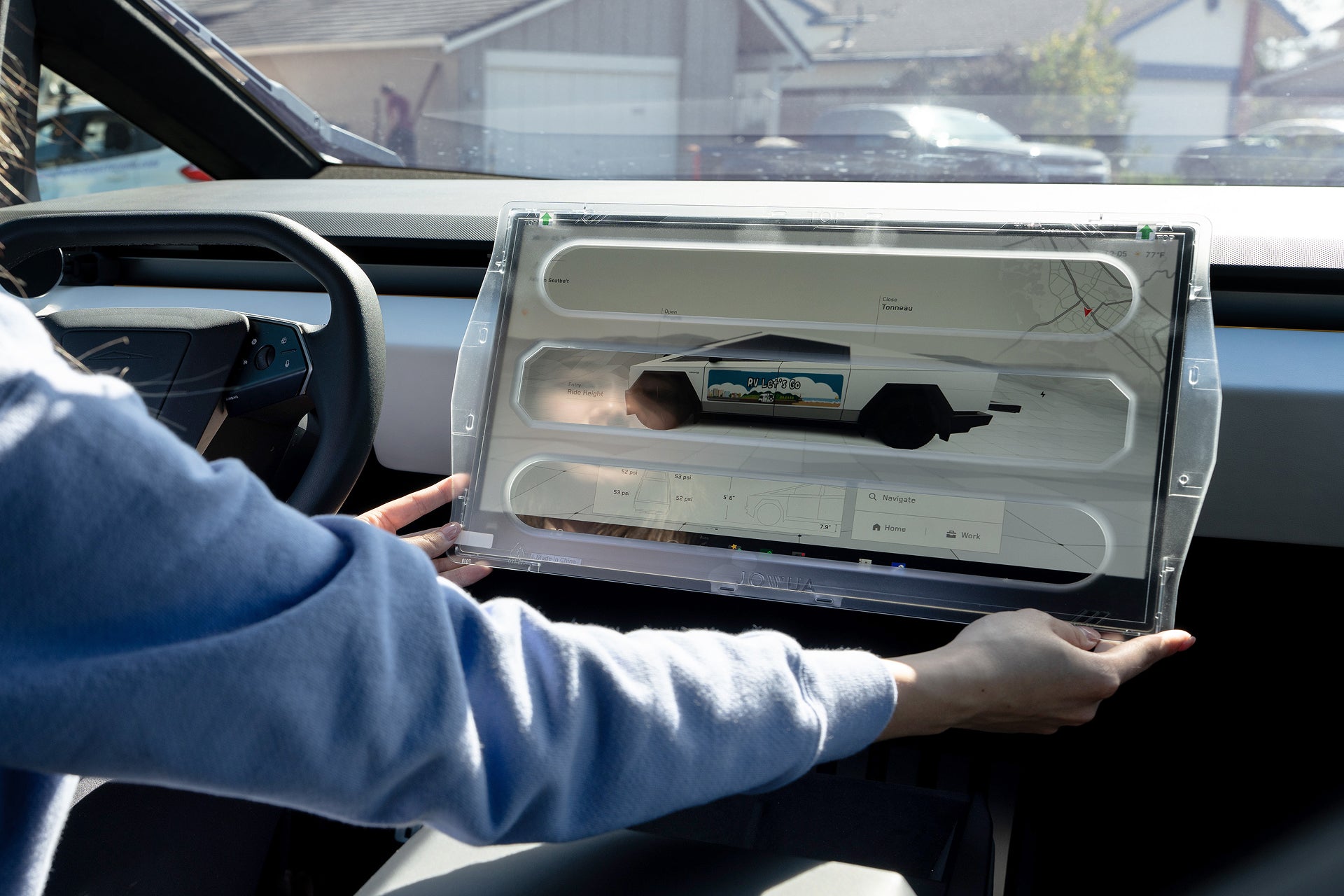 Inside a vehicle showing a map and truck image, someone adjusts the JOWUA Tempered Glass Screen Protector for Cybertruck. The 9H glass, held by two hands, shows a residential neighborhood through the windshield.