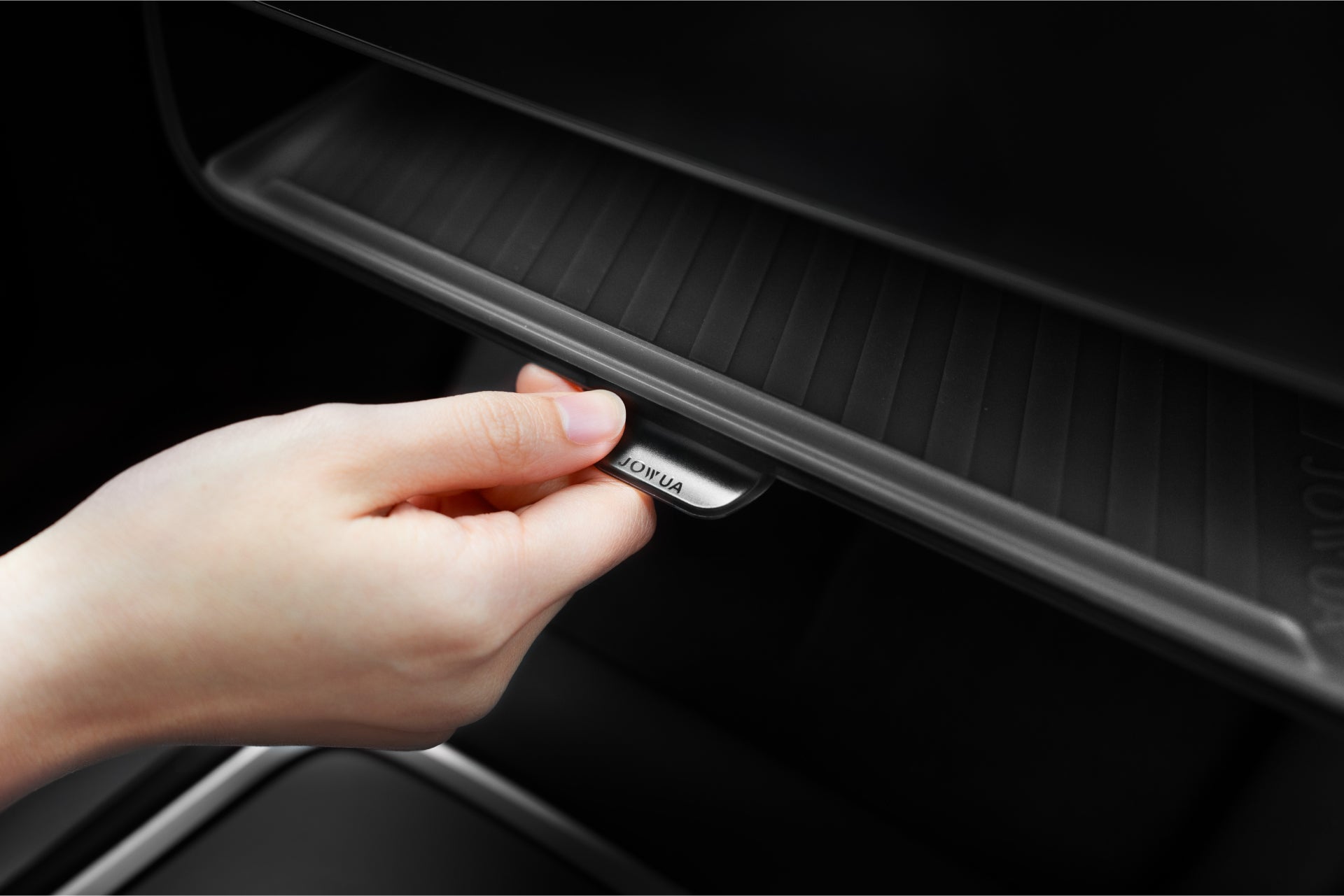 A hand opens a car's glovebox by pulling a small lever marked 