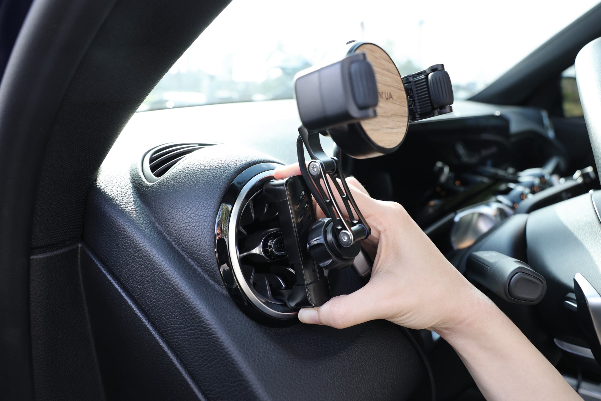 A hand adjusts the JOWUA Universal Air Vent Car Mount (Qi2 Universal Roller Mount) on a car's air vent, with the dashboard and steering wheel in view. This holder has silicone roller clamps and supports wireless charging for easy access while driving.