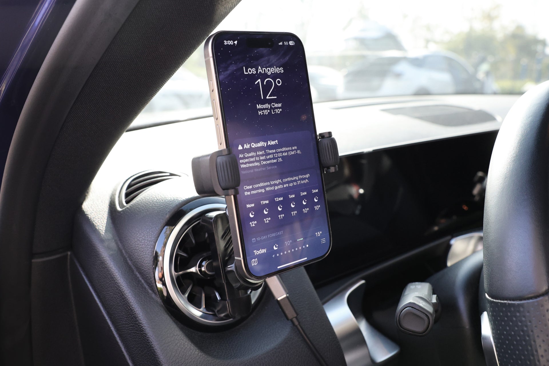 The JOWUA Universal Air Vent Car Mount (Qi2 Universal Roller Mount) securely holds a smartphone with wireless charging capability, displaying Los Angeles weather info on the car dashboard. The screen shows 12°C and an air quality alert, keeping drivers informed.