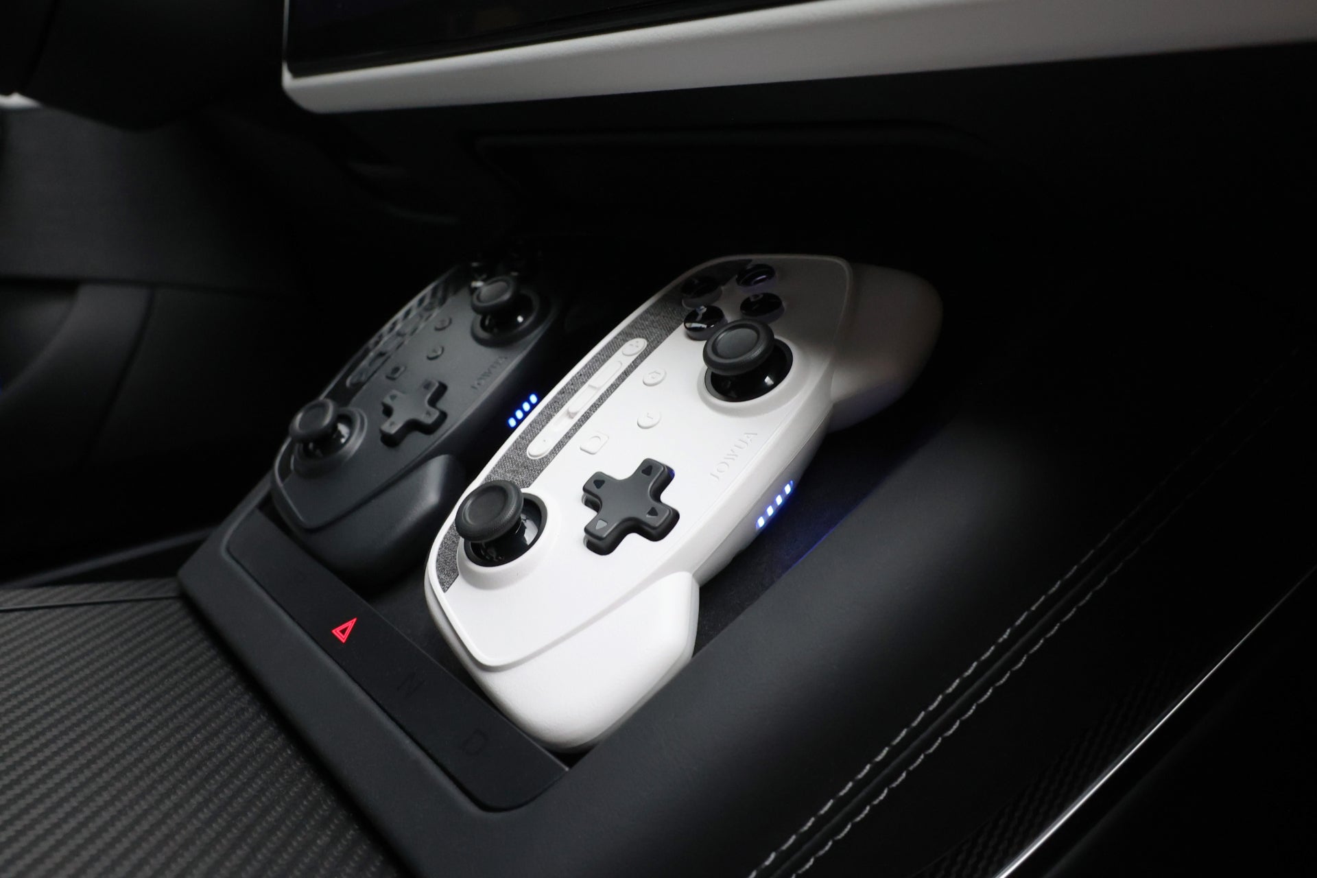 A close-up of a pair of JOWUA Wireless Tesla Game Controllers Combo (Model S/3/3HL/X/Y/Cyber) nestled in a car's center console, perfectly complementing the sleek design. The black and white controllers lie seamlessly, suggesting the potential for wireless charging and Bluetooth connectivity by Tesla Steam in a futuristic driving experience.