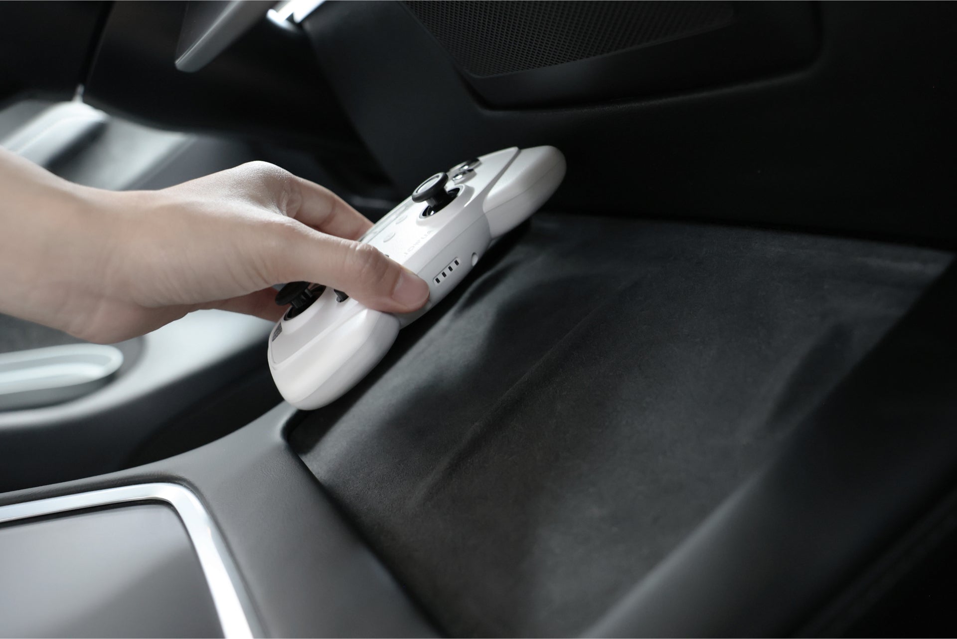 A hand placing a JOWUA Wireless Tesla Game Controller from the Reengineered Model 3 Highland, 2024+ Combo into the car's center console. The console, positioned between the front seats, includes a padded area that houses a USB Dashcam Hub, with the car's dashboard visible in the background.