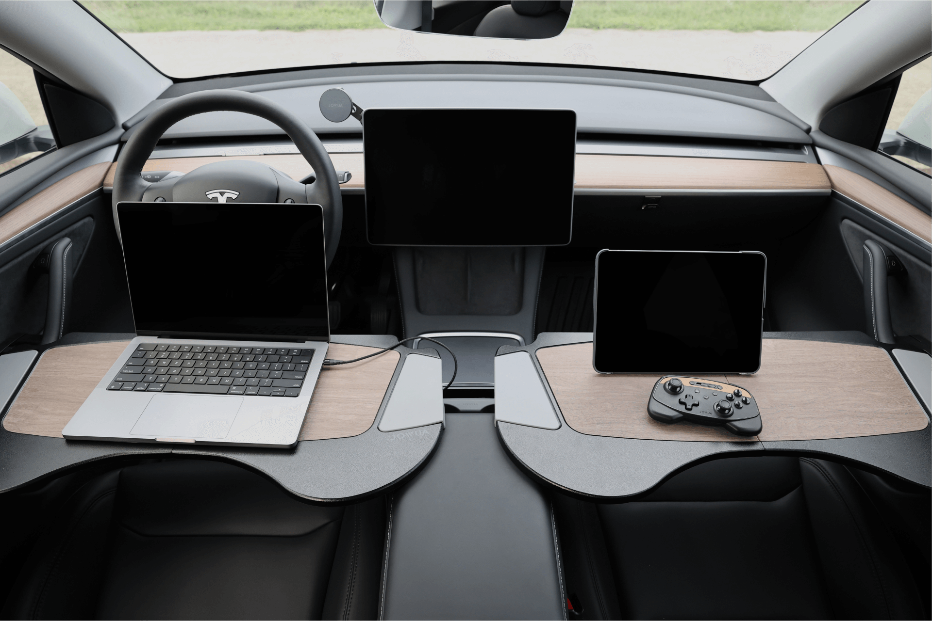 The interior of a modern car shines with elegant premium materials, including two JOWUA Foldable Car Trays for Tesla. One tray accommodates a laptop, while the other supports a tablet and gaming controller. The dashboard is equipped with a large central screen, complemented by Tesla Model X accessories.