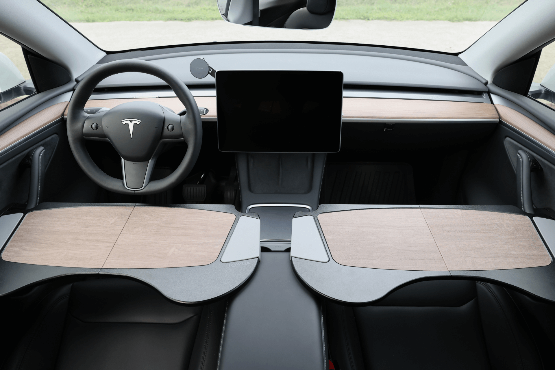 The interior of a Tesla is elegantly designed with high-end materials, offering a minimalist look that includes a large central touchscreen, wooden dashboard accents, and a sleek steering wheel adorned with the Tesla logo. The stylishly modern seats and surroundings can be further enhanced with optional accessories like the JOWUA Foldable Car Tray for Tesla Model S/3/X/Y.