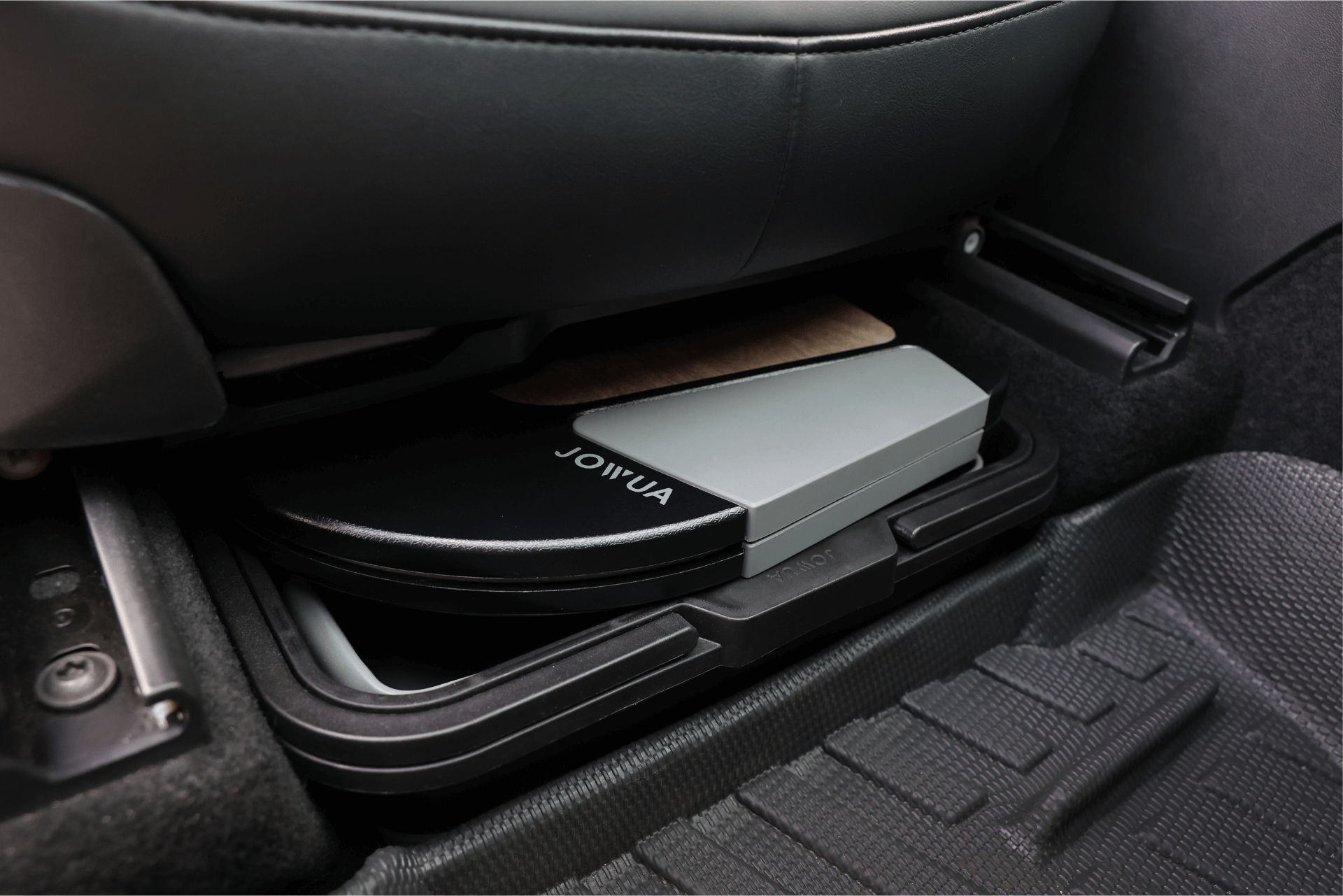 A sleek black and gray Foldable Car Tray from JOWUA is tucked under a car seat in a Tesla Model S, partially visible amidst the sophisticated car interior that boasts premium materials, textured flooring, and impeccably clean black seats.