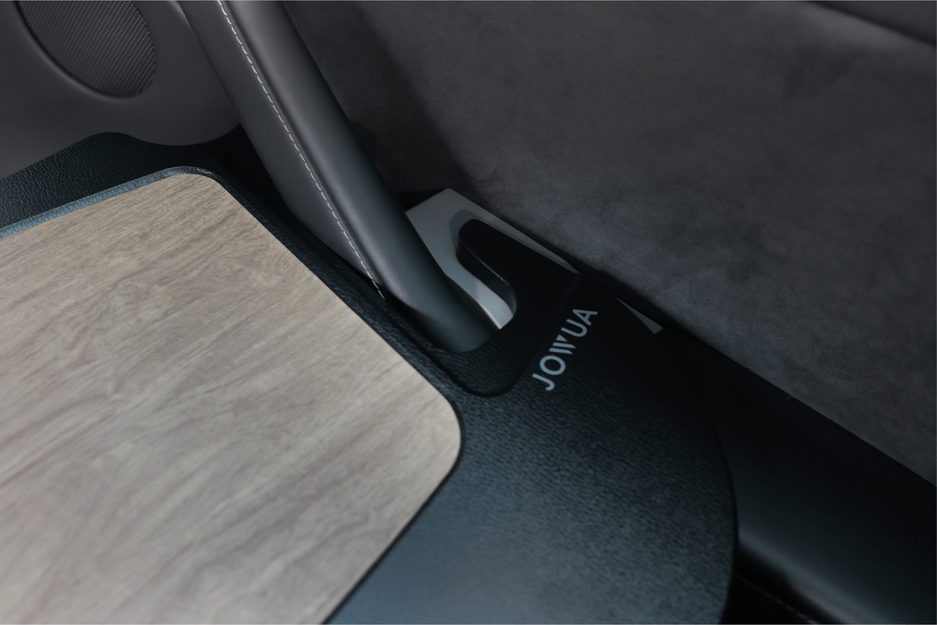 Close-up of a Tesla's interior featuring the Foldable Car Tray for Tesla, crafted with premium materials and supported by a gray structure. The word "JOWUA" is visible on the black base next to the tray, set against the backdrop of elegant gray upholstery.