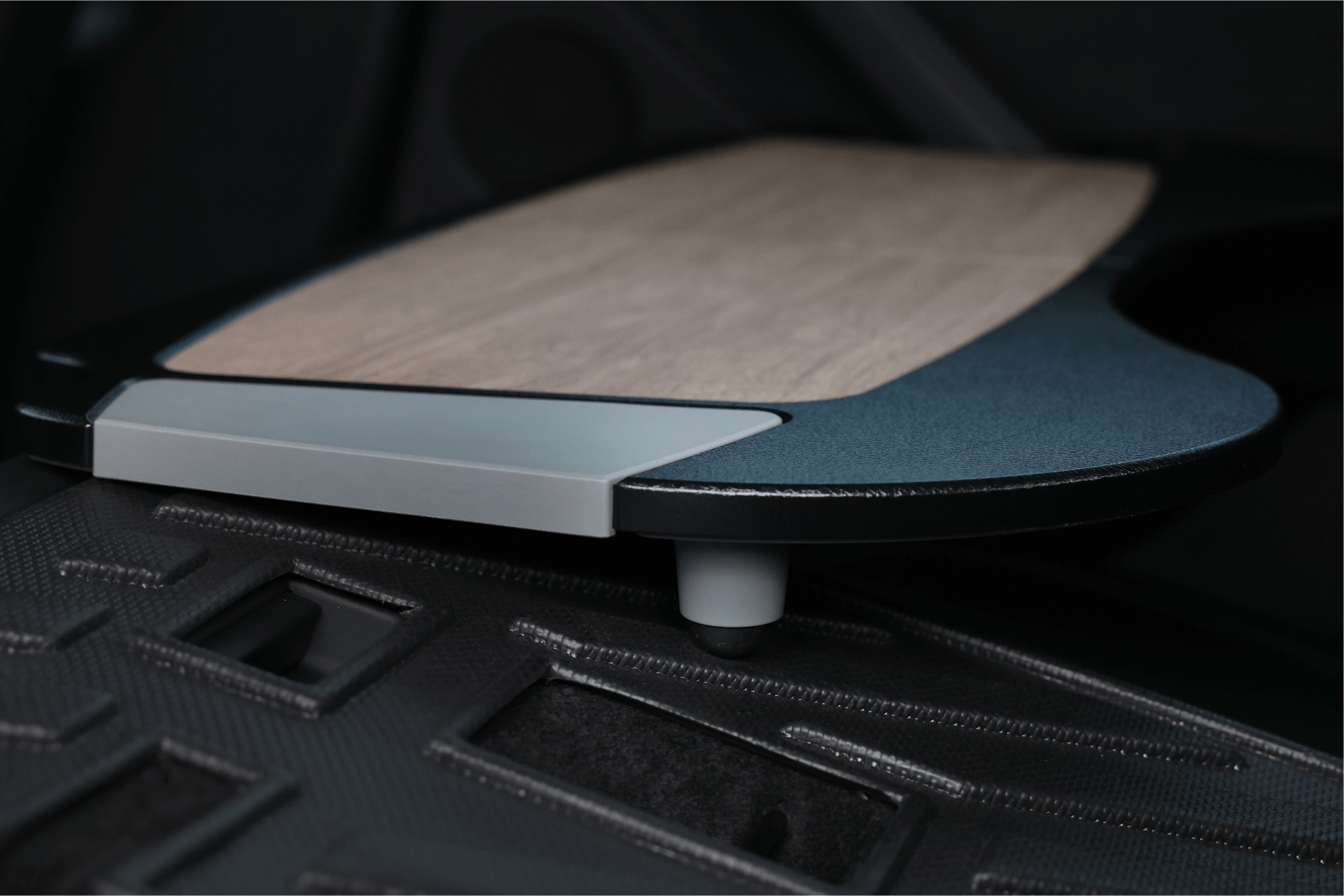 A close-up of a Tesla Model S interior highlights a JOWUA Foldable Car Tray, featuring a wood-like surface crafted from premium materials. This elegant tray is partially extended over a textured black panel, enhancing both convenience and functionality inside the vehicle.