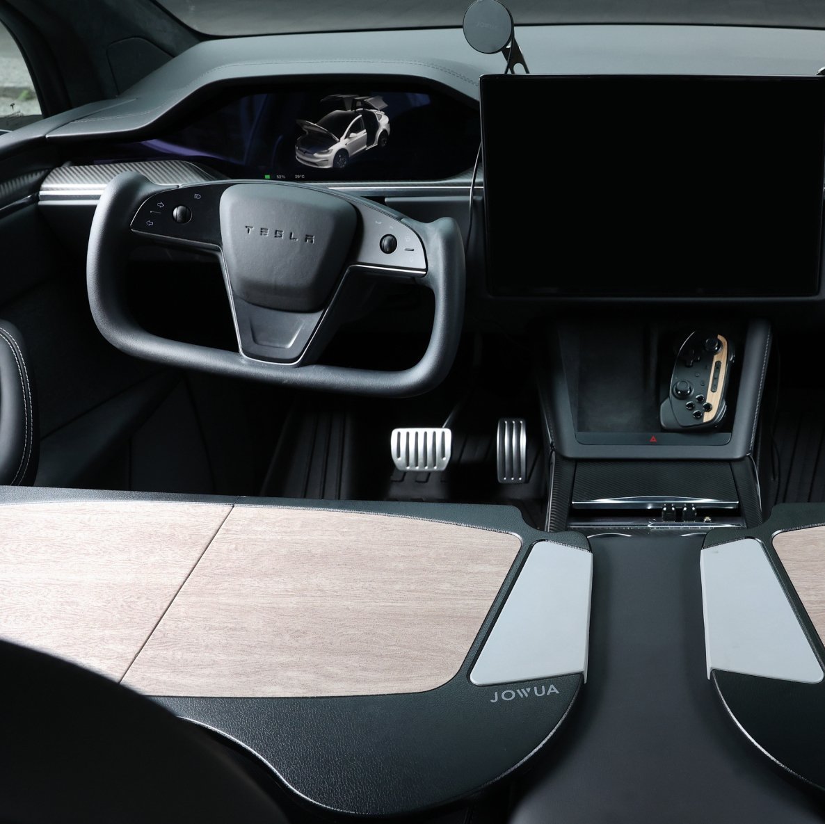 The image showcases the interior of a Tesla vehicle, emphasizing its minimalist dashboard complete with a yoke steering wheel and a large central touchscreen. Elegant wood panel accents complement the design, while three pedals stand ready for the driver. To elevate this experience, consider enhancing it with JOWUA's Tesla Christmas: The Ultimate Bundle of must-have accessories.