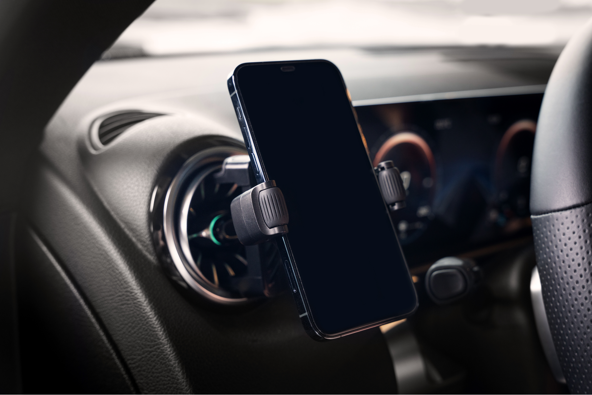 A smartphone is held securely in place using the JOWUA Universal Air Vent Car Mount, which features adjustable clamps. The car's dashboard and steering wheel are partially visible, enhancing the modern and sleek interior aesthetic. This phone holder offers 360-degree rotation for optimal viewing angles, even when the screen is turned off.