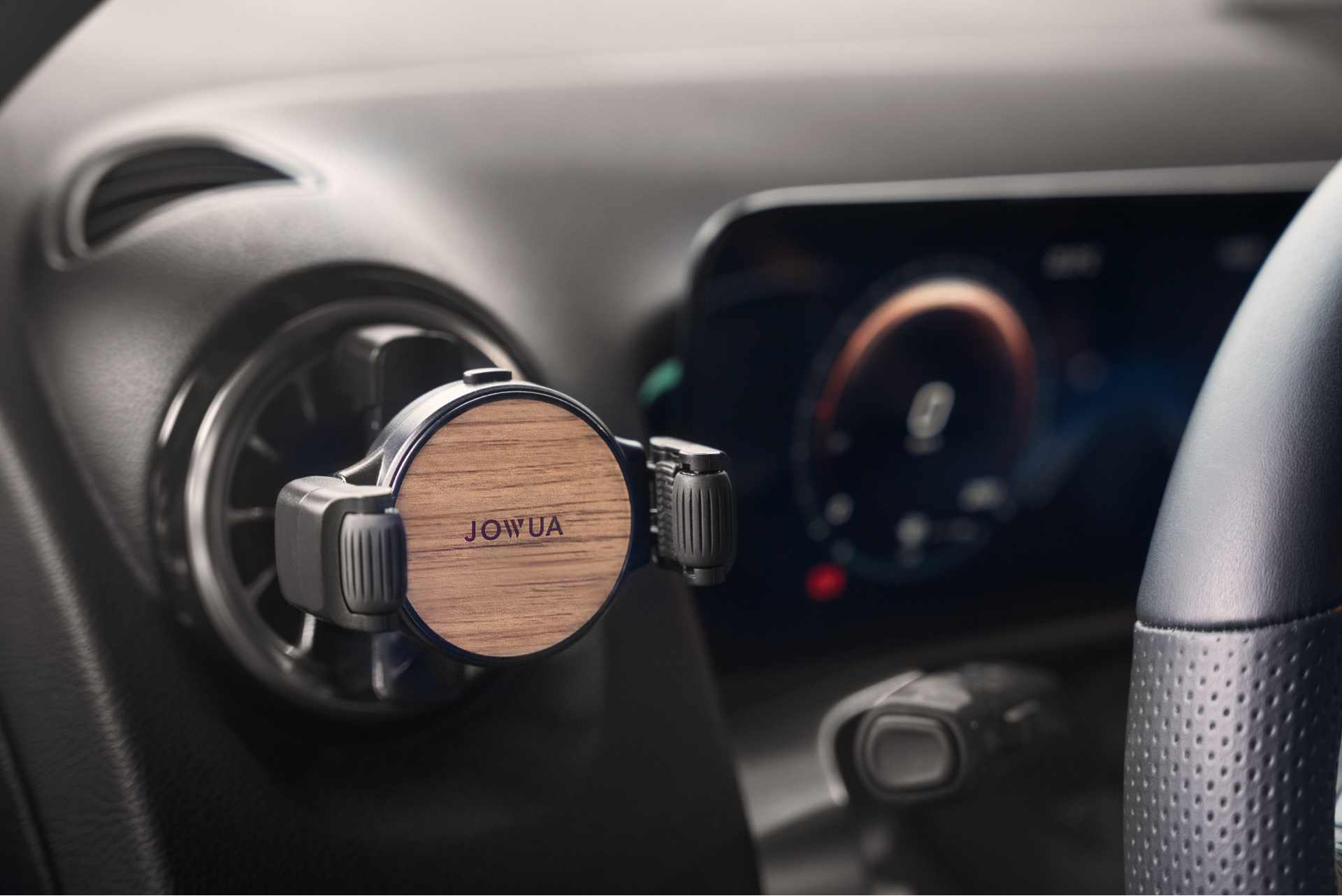 A wooden Universal Air Vent Car Mount with adjustable clamps is prominently displayed on the car's air vent, allowing for 360-degree rotation and proudly featuring the "JOWUA" brand. The background includes a digital display and a steering wheel, enhancing the sleek design.